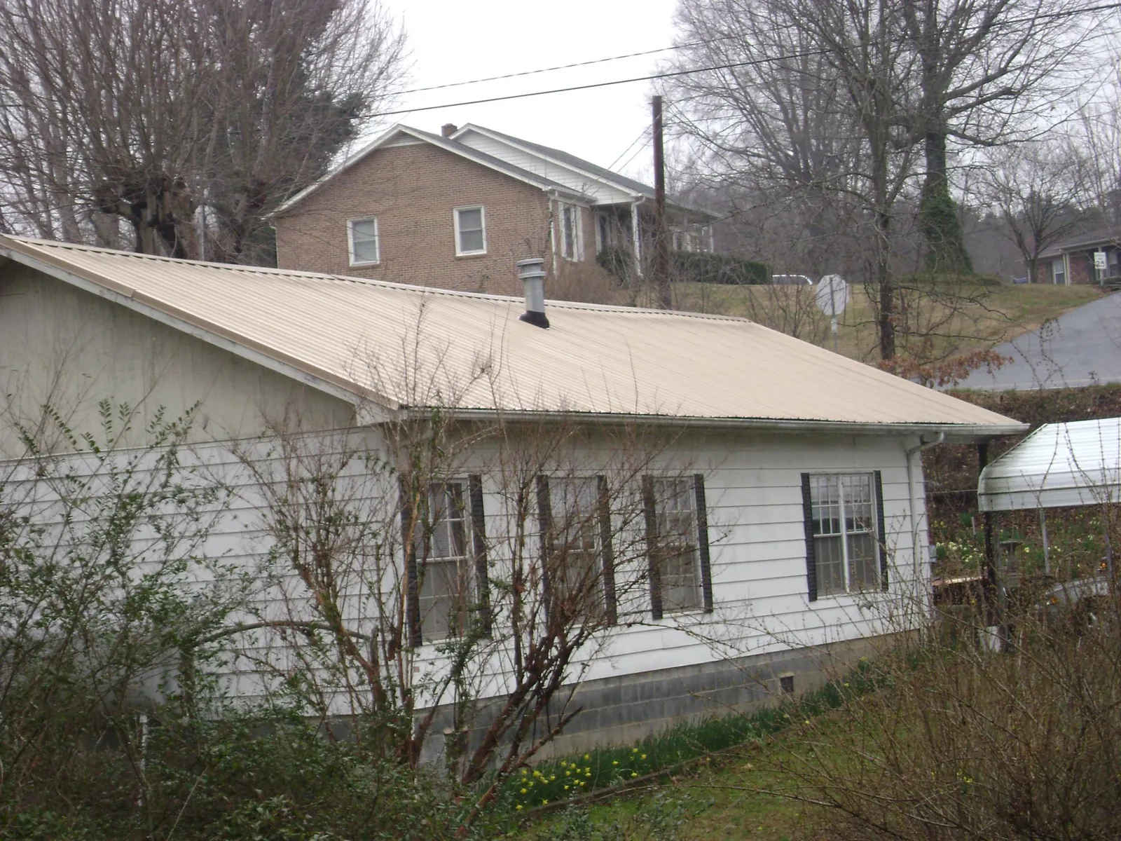 Tan metal roof on a white sided house set into a hillside — Commercial Roofing by Roofing Brothers in Hollywood